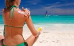 Green bikini girl sitting on the beach putting on sunscreen