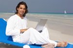 man sitting on loung chair at the beach wearing all white with laptop