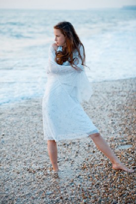 girl wrapped in white shawl standing by the ocean